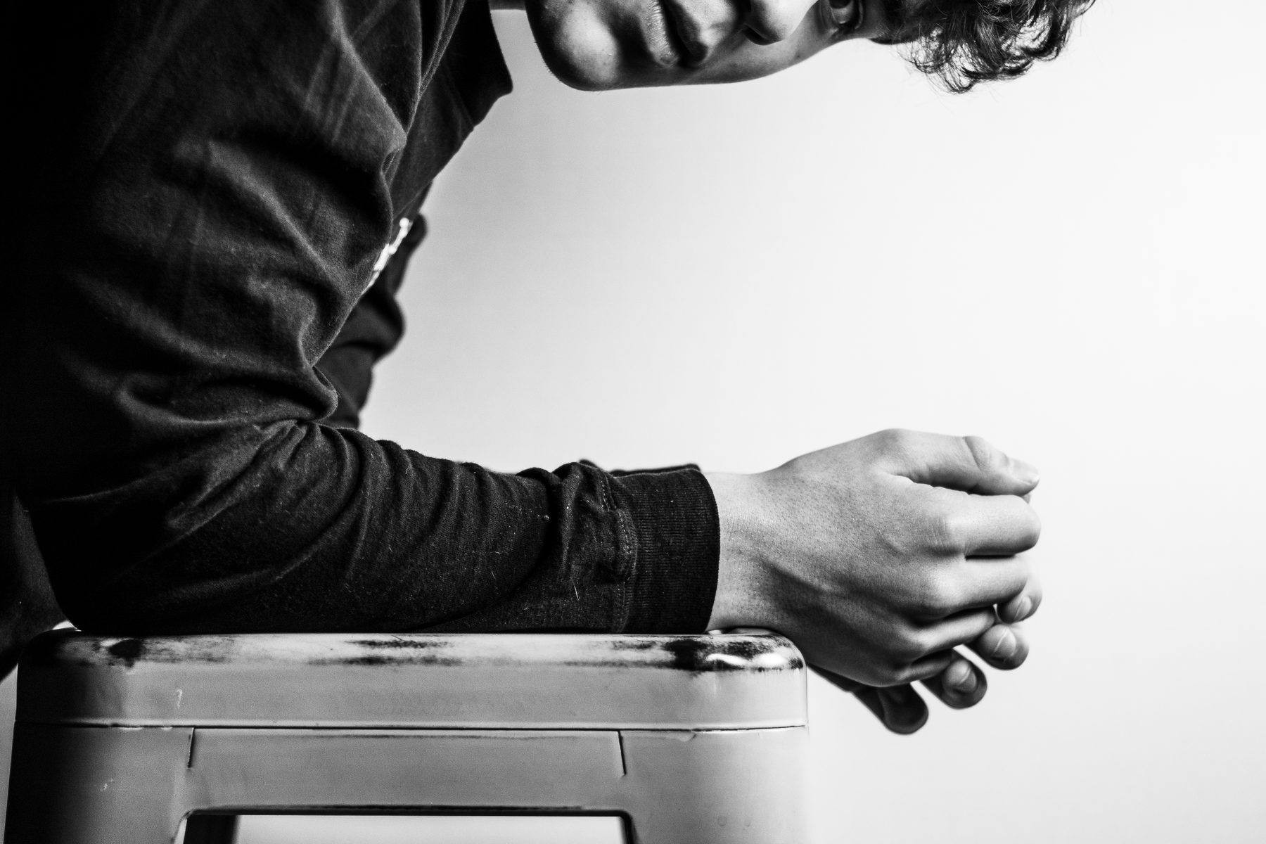 Leaning on a studio stool, hands clasped
